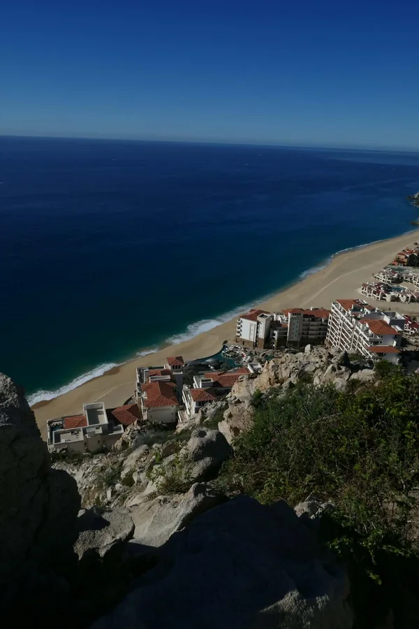 Blue ocean and a sandy beach below a rocky overlook and coastal buildings
