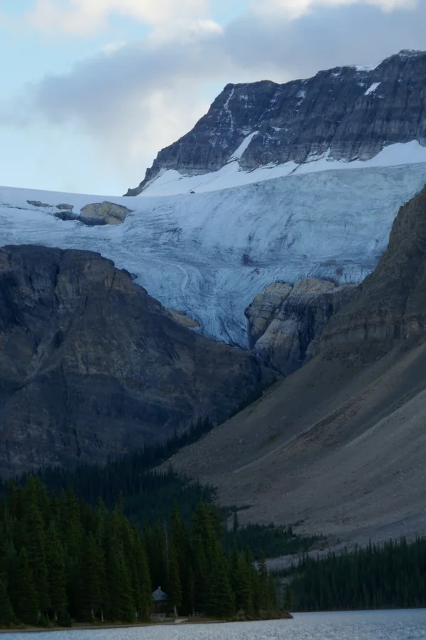 Glacier spilling down a mountain face above a forested lakeshore