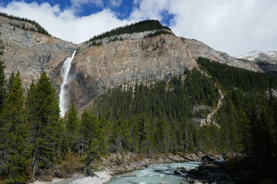 Tall waterfall dropping from a limestone cliff beside a turquoise river